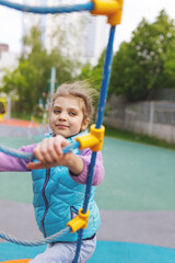 happy smiling cheerful girl 6 years old clinging to rope ladder, children's sport at playground