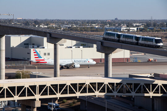 PHX Sky Train on Bridge and an American Airlines Airbus A321 just beyond on a taxiway at Phoenix Sky Harbor International Airport - Phoenix, Arizona, USA