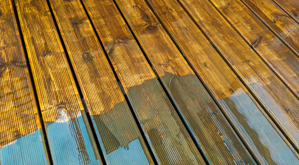 Wet and being cleaned old wooden brown terrace decking with the old paint layer partially removed