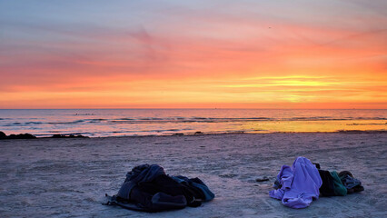A towel, a hand bag and a beach bag lie on the sandy beach. Set of personal items at sunset.