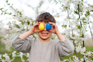 Happy easter. Cute funny preschooler boy with Easter eggs in garden, portrait against background of...