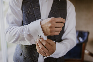 Close up of man with waistcoat and white shirt adjusting his cufflinks