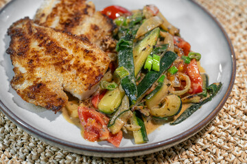 Healthy fish dish of fried redfish fillet with Mediterranean vegetables such as zucchini, tomatoes and leek in sauce, high protein meal for low carb or ketogenic diet, copy space