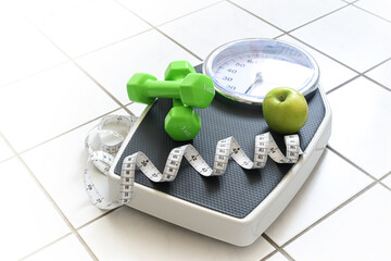 Fitness and weight loss concept, personal scale with measuring tape, green dumbbells and an apple...