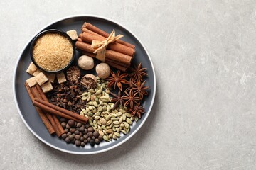 Plate with different aromatic spices on light textured table, top view. Space for text