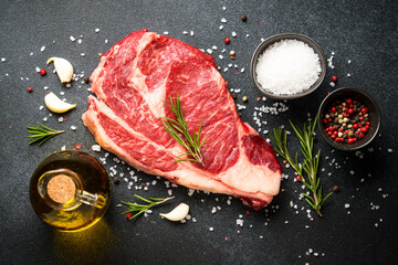 Meat steak. Beef steak ribeye with spices and herbs on black background. Top view with copy space.