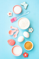 Easter baking background on blue. Flour, edds, sugar and gingerbread cookies. Top view with copy space.