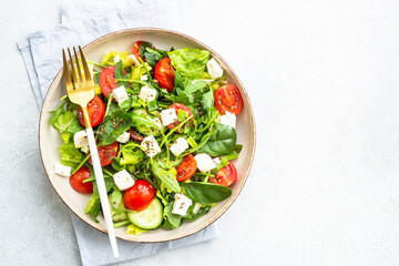 Green salad with spinach, arugula and tomatoes with olive oil. Top view on white.