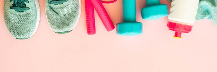 Fitness equipment on pink background, flat lay image. Sneakers, dumbbells, towel and bottle of water. Long banner format.