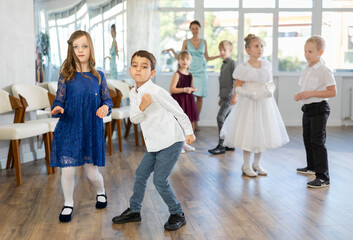 Excited preteen children, boy and girl in party attire artistically performing twist in sunny dance...