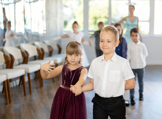 Group of cheerful emotional tweens, girls ad boys in formal wear dancing slow romantic partner dance in sunlit classroom during children festive event