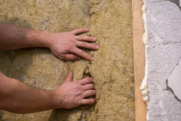Precision Placement: Man Elevates Insulation with Careful Insertion of Mineral Wool into Notch.