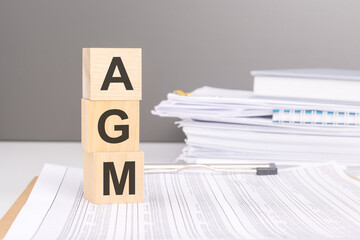 AGM - Annual General Meeting acronym, wooden blocks, business concept gray background, financial document.