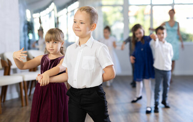 Merry junior schoolchildren in party dresses lined up in pairs during waltz dance in social hall