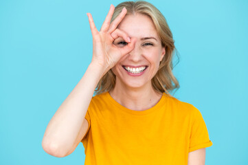 Portrait of smiling young woman peeping through ok gesture - obrazy, fototapety, plakaty