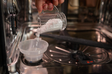 High-angle view of unrecognizable man using funnel to pour granulated salt to soften hard water...