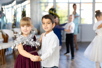 Enthusiastic preteen children, girls and boys in elegant outfits practicing partner dance moves in...