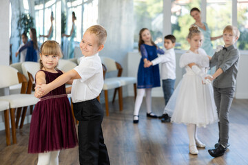 Enthusiastic preteen children, boys and girls in party attire performing elegant waltz in pairs in...