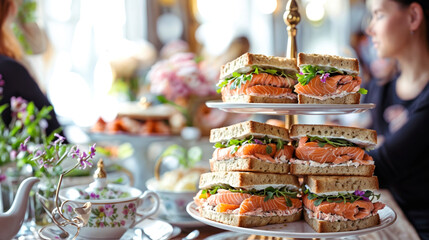 old fashioned tea shop on table, salmon and cucumber sandwiches with cake on a cake stand. two people sitting at the table