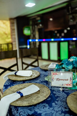 a round table decorated with a blue tablecloth, plate holder and a flower arrangement with a glass vase