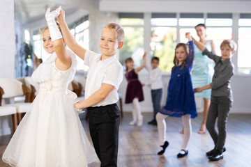 Enthusiastic preteen children, boys and girls in party attire performing elegant waltz in pairs in...
