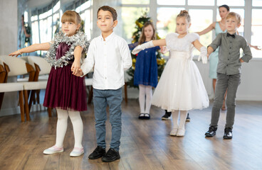 Group of preteen children in festive clothes dances waltz around a Christmas tree