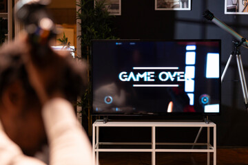 Man playing videogames on TV after long day at work angry after receiving game over screen. Gamer...