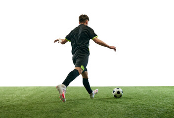 Fototapeta premium Young man, football player in uniform playing, training, dribbling ball isolated over white background with grass flooring. Concept of sport, game, competition, championship, active lifestyle