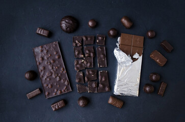 Sweet temptation: two chocolate bars and delicious chocolates on a dark background.  Flat lay, top view.  A combination of milk and dark chocolate.