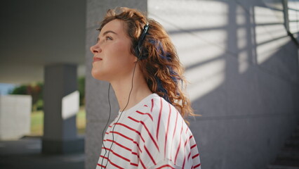 Stylish hipster listening headphones music closing eyes on sunny street close up