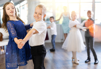 Happy interested preteen pupils preparing for festive school event, rehearsing ballroom dance steps...