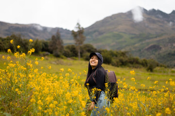 Fototapeta na wymiar Exploradora de la naturaleza urbana Una chica atractiva con mochila entre flores amarillas. Estilo de vida, turista viajera