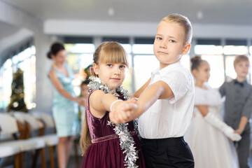 Obraz premium Joyful minor schoolboys and schoolgirls training valse dance in events salon adorned with Xmas tree