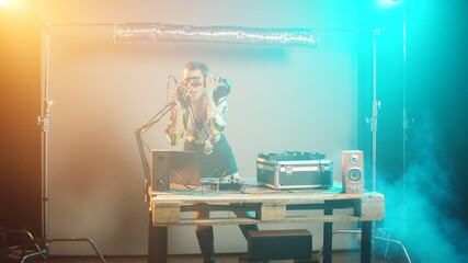 Cool DJ with crazy makeup mixing tunes at turntables, using audio equipment to play modern remix music. Joyful funky woman playing techno songs on electronics buttons. Handheld shot.