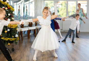 Joyful minor schoolboys and schoolgirls training valse dance in events salon adorned with Xmas tree