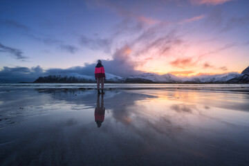 Woman on the beach, snowy mountains and colorful sky at sunset