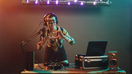 Cool performer mixing music and showing heart shape sign during techno party, funky woman with...
