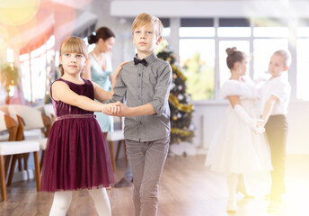 Enthusiastic preteen children, girls and boys in elegant outfits practicing partner dance moves in...