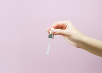 female hand holding a pipette with serum on a pink background. skin care concept