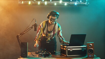 Young musician acting cool looking at mixer, focused on bass control buttons at turntables equipment over smoky background. Working with audio equipment to mix sounds. Tripod shot.