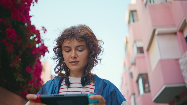 Young woman playing nintendo switch console walking summer street close up