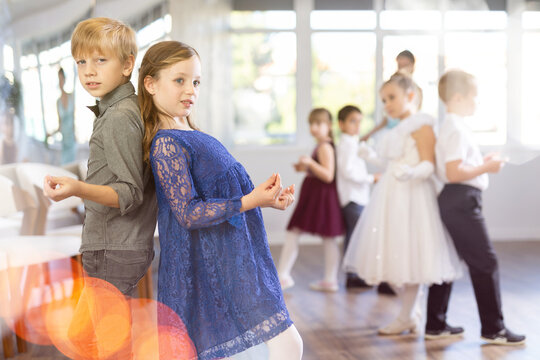 Smiling junior schoolchildren in party dresses learning dancing rock and roll with pedagogue in social hall