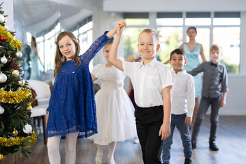 Christmas ball - beautifully dressed children dance the Viennese waltz near the New Year tree