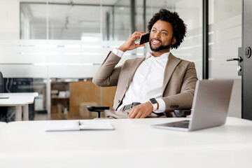 A poised African-American businessman is engaged in a phone conversation in a modern office...