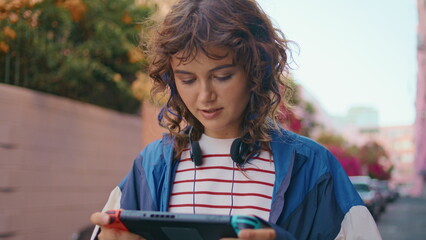 Teen enjoy portable video game on street close up. Girl focused handheld console