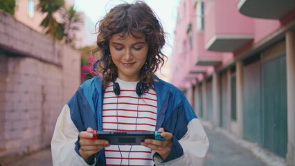 Naklejka premium Teenager playing handheld console walking urban area. Woman focused on display 
