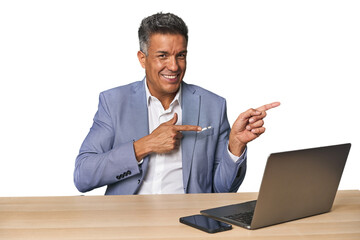 Elegant businessman at desk with laptop excited pointing with forefingers away.