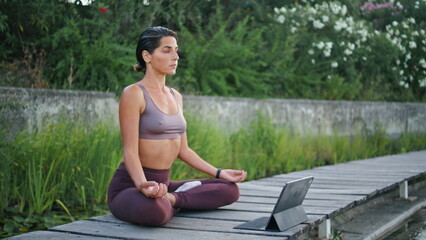 Fototapeta na wymiar Calm lady sitting lotus position park bench. Woman watching online yoga lesson