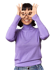 Young Hispanic woman with short black hair in studio showing okay sign over eyes