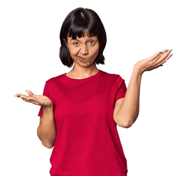 Young Hispanic woman with short black hair in studio doubting and shrugging shoulders in questioning gesture.